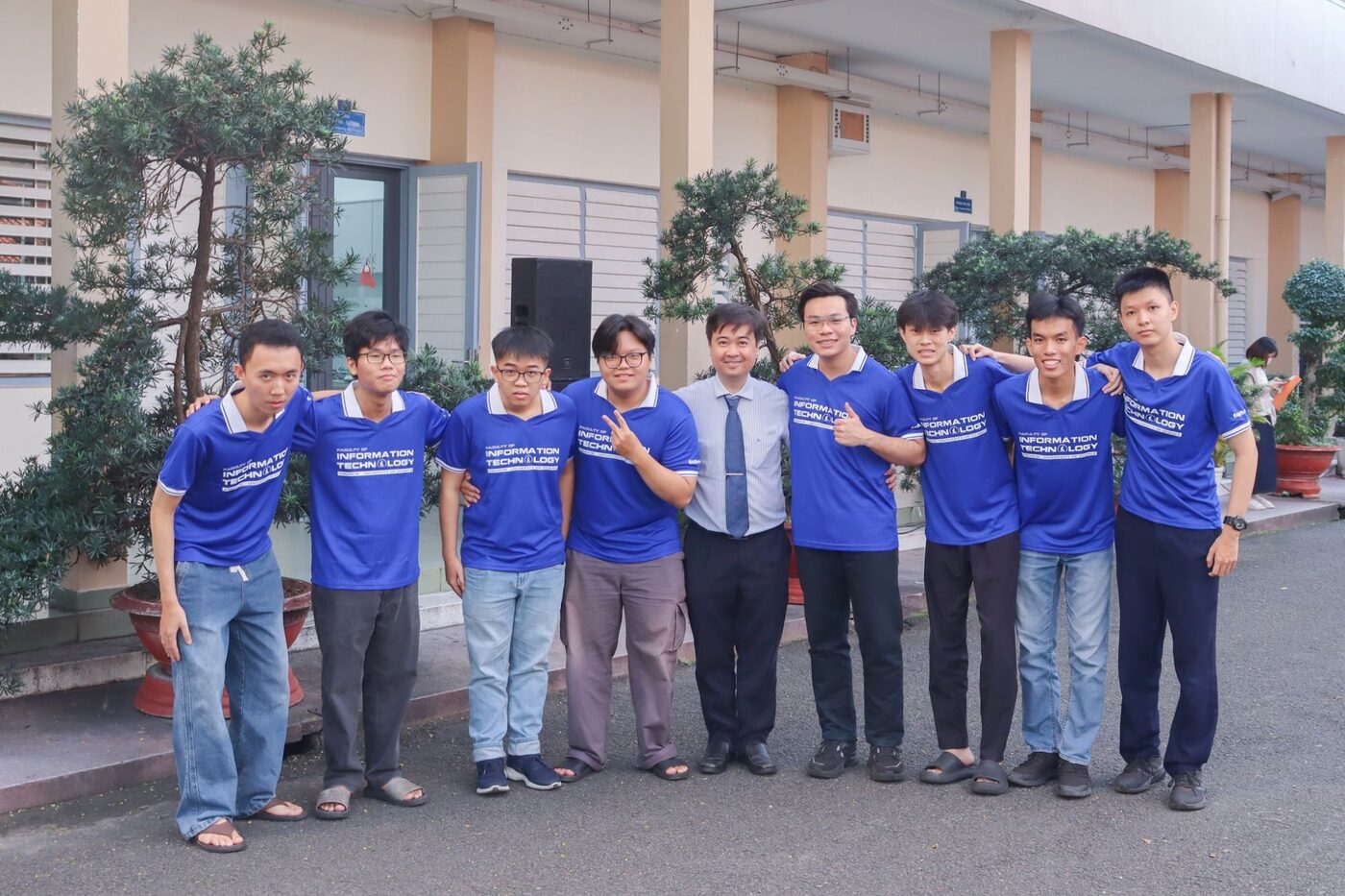 The contest squad in Faculty of Information Technology polo shirts, lined up with a member of the faculty outside the department building