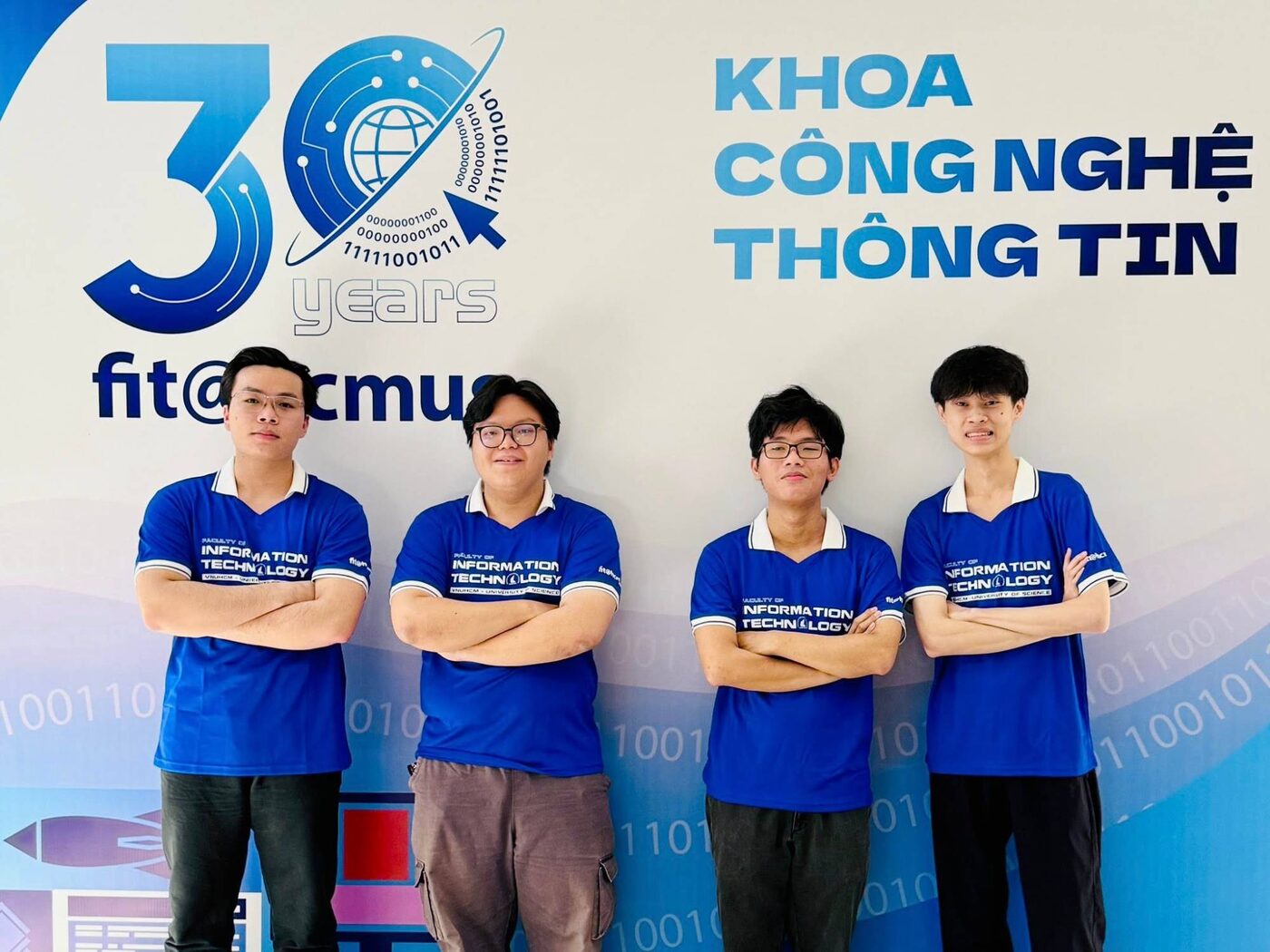 Four team members in Faculty of Information Technology polo shirts in front of the faculty's thirtieth-anniversary backdrop